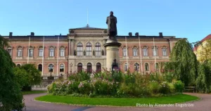 The image depicts a grand building at Uppsala University, showcasing classic architectural design. The edifice features a symmetrical façade with arched windows on the ground floor and rectangular windows on the upper floors, all framed with decorative moldings.