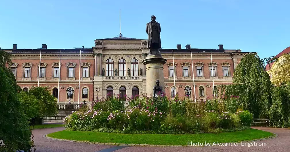 The image depicts a grand building at Uppsala University, showcasing classic architectural design. The edifice features a symmetrical façade with arched windows on the ground floor and rectangular windows on the upper floors, all framed with decorative moldings.
