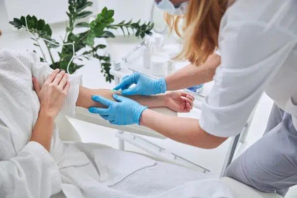 The image depicts a healthcare professional in the process of collecting a blood sample from a patient. The professional is wearing blue gloves and a surgical mask, following proper sanitary protocols to ensure a sterile environment.