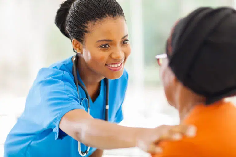 L'image représente un établissement de soins où une jeune femme, vêtue d'une blouse bleue et d'un stéthoscope autour du cou, tient les mains d'un patient plus âgé.