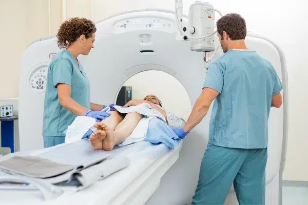 Cette image montre un examen TEP (tomographie par émission de positons) en cours dans un établissement médical. Le patient est allongé sur un lit étroit qui fait partie de l'appareil de TEP.