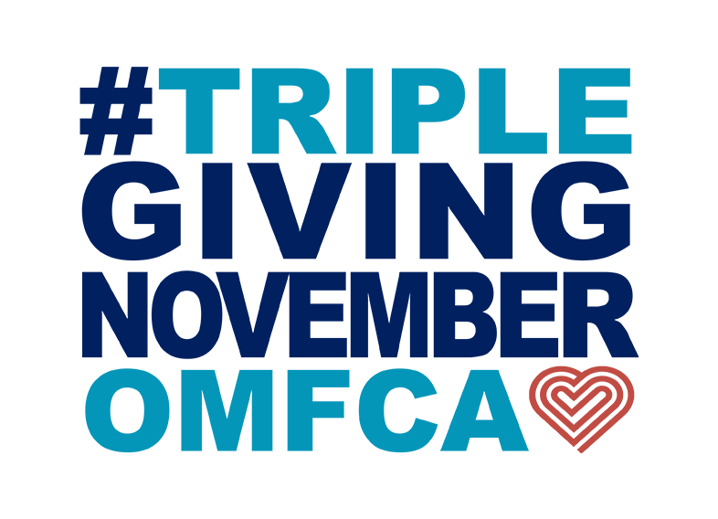 TGN logo: #TRIPLEGIVINGNOVEMBEROMFCA. The phrase is written in bold, uppercase letters with a mix of dark blue and light blue colors. The "OMFCA" text is in light blue, and there is a stylized heart shape in reddish-orange next to it.